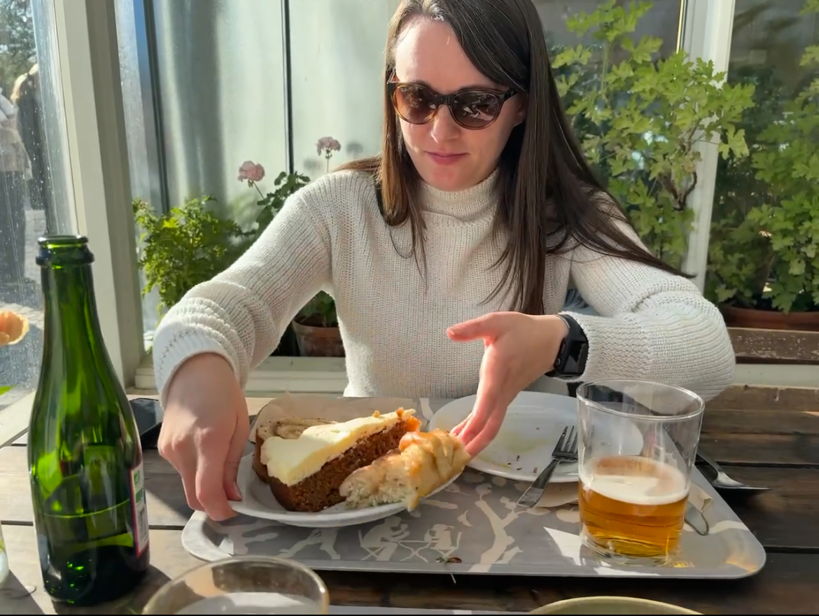A smiling woman seated at a restaurant table with a slice of cake on a plate in front of her.