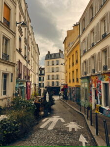 Colorful street in the Montmartre neighborhood of Paris, lined with charming buildings, greenery, and cobblestone pavement.
