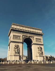 Arc de Triomphe in Paris under a bright blue sky, highlighting its detailed carvings and grand architecture.