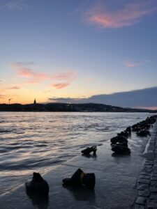 Bronze shoe memorial on the Danube River bank at sunset in Budapest, honoring Holocaust victims with warm golden light reflecting on the water.