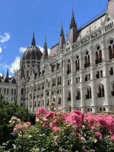 Hungarian Parliament Building on a sunny day, framed by vibrant pink flowers and a clear blue sky.”