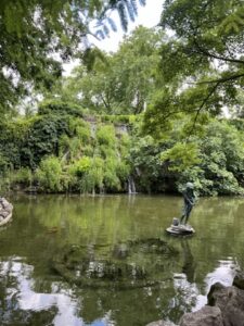 Tranquil pond with a statue at its center on Margaret Island in Budapest, surrounded by lush greenery and peaceful walking paths.