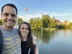Couple smiling in front of a colorful hot air balloon with Vajdahunyad Castle in the background, captured in Budapest’s City Park.