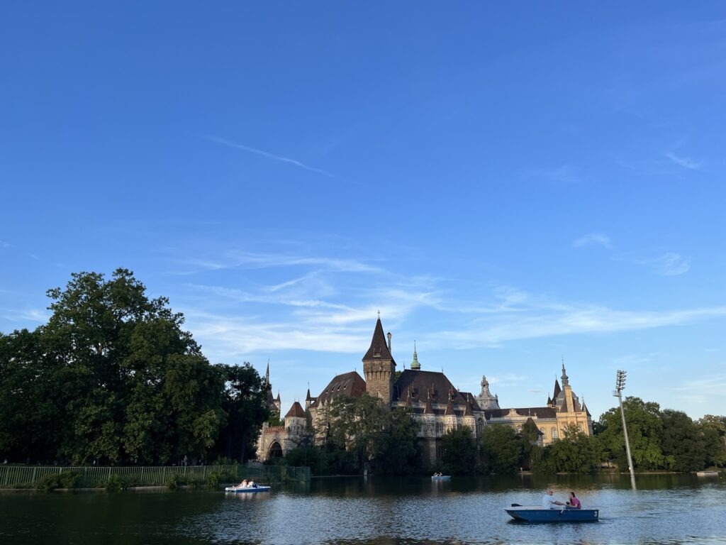 Vajdahunyad Castle reflected in the river at City Park in Budapest, showcasing its mix of Gothic and Romanesque architecture surrounded by greenery.