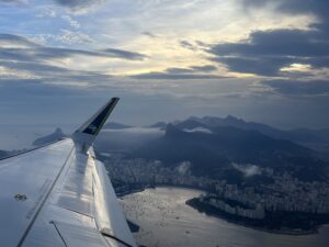 Aerial view of Rio de Janeiro mountains from airplane window, with plane wing visible, traveling in Brazil.